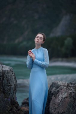 Mavi elbiseli bir kız nehir kıyısındaki kayalık bir sahilde duruyor. Akşamları nehir kenarında. Altai 'de fotoğraf çekimi