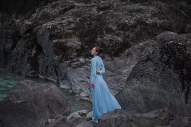 Mavi elbiseli bir kız nehir kıyısındaki kayalık bir sahilde duruyor. Akşamları nehir kenarında. Altai 'de fotoğraf çekimi