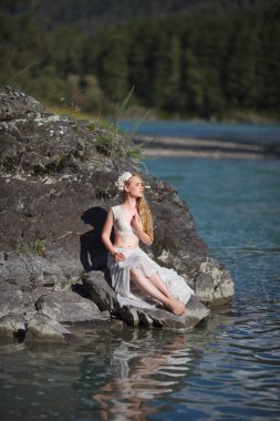 Deniz Kızının Hikayesi. Nymph Nehri 'nin Hikayesi. Beyaz elbiseli bir kız nehir kenarındaki kayalık bir sahilde duruyor. Altai 'de fotoğraf çekimi.