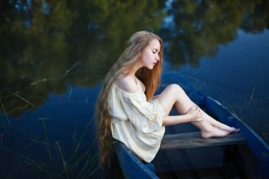 Batık bir teknede oturan uzun saçlı sarışın, melankolik, depresyonlu.