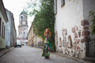 beautiful red-haired girl walks along the old streets of Vyborg clipart