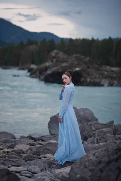 一个身穿蓝色衣服的女孩站在河边的岩石海岸上 晚上在河边 阿尔泰的照片传送 — 图库照片