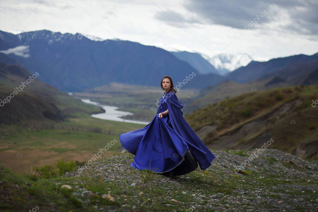 A girl in a magnificent blue dress walks in the mountains.