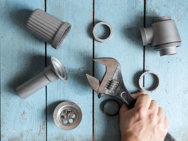 Tesisat işindeyim. Sorun giderme işlemi eski mavi ahşap bir masada yapılır. Eldivenli bir işçi soğuk sıcak su musluğunu çeviriyor. Böylece çöküşü ortadan kaldırırız.