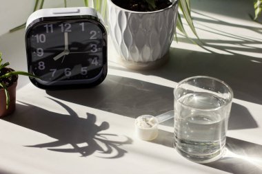 Fish collagen peptides powder and glass of water. alarm clock near spoon with collagen.