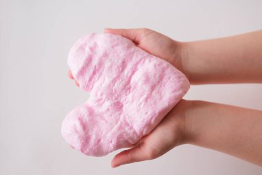 Pembe balçık ya da çocukların elindeki sakız oyuncağı. Kalp şeklindeki tüylü balçık DIY projesi. Boş zaman ve ev yapımı oyuncaklar konsepti. Karantina sırasında kapalı etkinlikler.