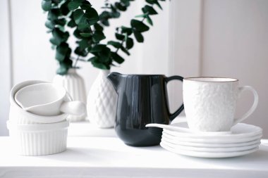 Beyaz fincan, tabak, çay tabağı ve süt sürahisi beyaz bir masada. metin için boşluk kopyala. Taze ve asgari mutfak tarzı. Temiz ve dağınık bir oda. İskandinav tasarımı. 