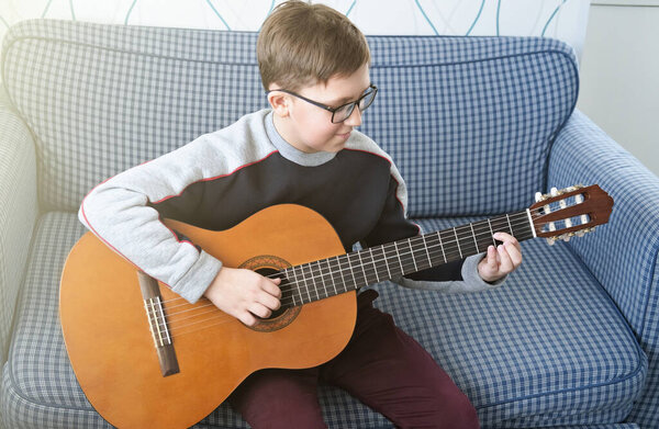 Learning to play the guitar. Music education. boy playing acoustic guitar. serious teenager in glasses trying to play indoors.