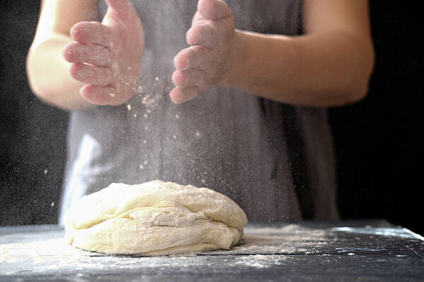 Making dough by hands at bakery or at home. Flour cloud in the air.