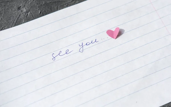see you note hand written on a paper. love letter with paper heart. relationship concept. distance relationship or long parting. missing love or partner. romantic reminder