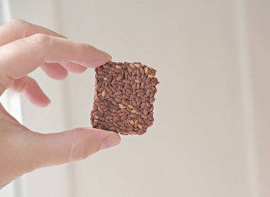 hand holding crunchy multigrain cereal flax seed crispbread. squares bars for healthy snack. energy bars with no sugar added.  clipart