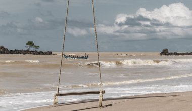 Arka planda balıkçı teknesi olan boş bir sahilde salıncak ve balıkçı teknesi Axim Gana Batı Afrika 'da..