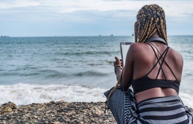 Önünde Batı Afrika Denizi 'nin önünde cep telefonu olan Afrikalı bir kadın oturuyor. Fotoğraf Sekondi-Takoradi Gana 'da çekildi. 30 Ekim 2018