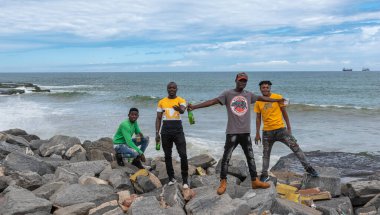 Parti adamları ellerinde birayla kayaların üzerinde duruyor ve 14 Eylül 2019 'da Takoradi Gana Batı Afrika' da hayatın tadını çıkarıyorlar.