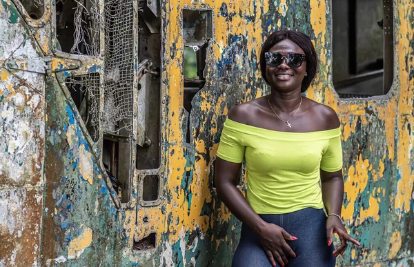 Happy Africa woman from Ghana stands in front of an old broken helicopter, which stands in the northern part of Accra Ghana West Africa