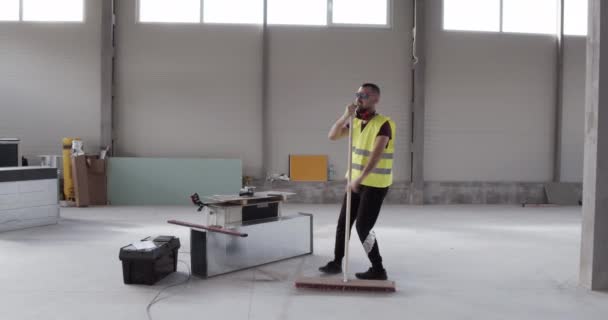 Un travailleur joyeux et bien disposé danse avec la balayeuse tout en nettoyant le dépôt .