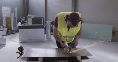 Metal bir depoda çalışan bir inşaat işçisi. Metal kesme makinesiyle bir yaprak kes.