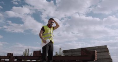 Çalışan bir adam, mühendis, elinde planla şantiyede yürüyor ve işlerin gidişatını kontrol ediyor. İnşaat yatırımları.