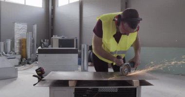 Metal bir depoda çalışan bir inşaat işçisi. Metal kesme makinesiyle bir yaprak kes.