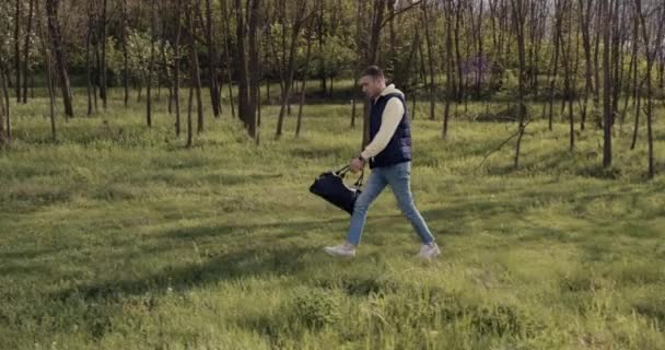 Un jeune homme marche dans le parc, vêtu avec désinvolture et un sac à la main — Video