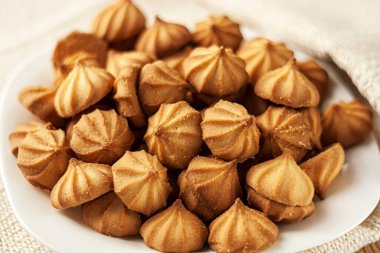 Beyaz masa örtüsü üzerinde beyaz tabakta kurabiyeler.