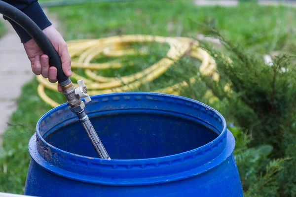 Suyu plastik fıçılarda hortumla dolduran insan eli.