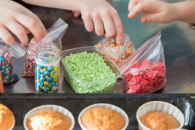 Çocuklar kurusıkı kapkekleri renkli hamur işleriyle süsler. 
