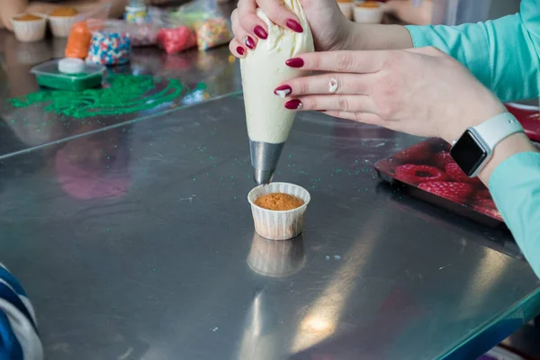 Feche mãos do cozinheiro com o saco de doces que aperta a nata em cupcakes — Fotografia de Stock