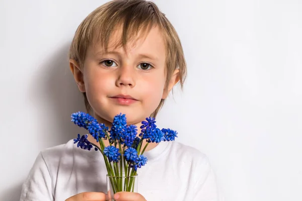 Portret pięknego dziecka posiada bukiet niebieskich kwiatów dla swojej matki. — Zdjęcie stockowe