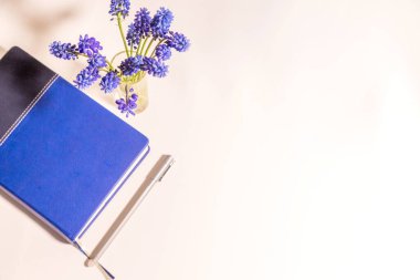 Mavi çiçekler beyaz masada ve kalem üst görüşlü günlükte.