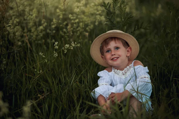 Menina bonito em um vestido branco e chapéu no campo na hora do pôr do sol — Fotografia de Stock