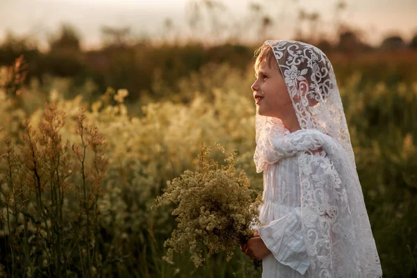 Menina bonito em um vestido branco e chapéu no campo na hora do pôr do sol — Fotografia de Stock