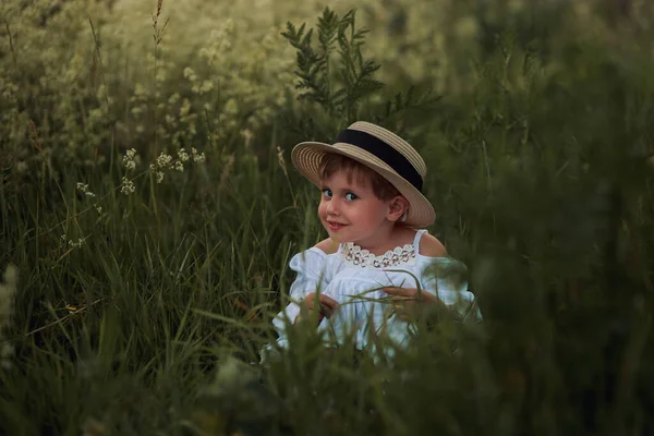 Linda niña en un vestido blanco y sombrero en el campo al atardecer — Foto de Stock