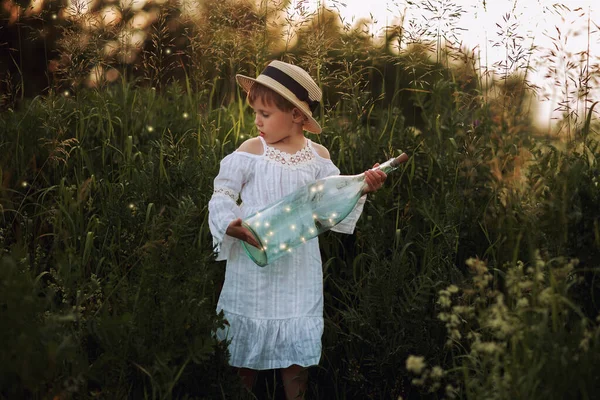Linda niña en un vestido blanco y sombrero en el campo al atardecer — Foto de Stock