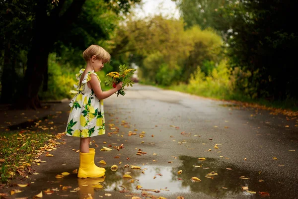 Pequena menina loira em um vestido colorido com uma lata de rega amarela sorrindo — Fotografia de Stock