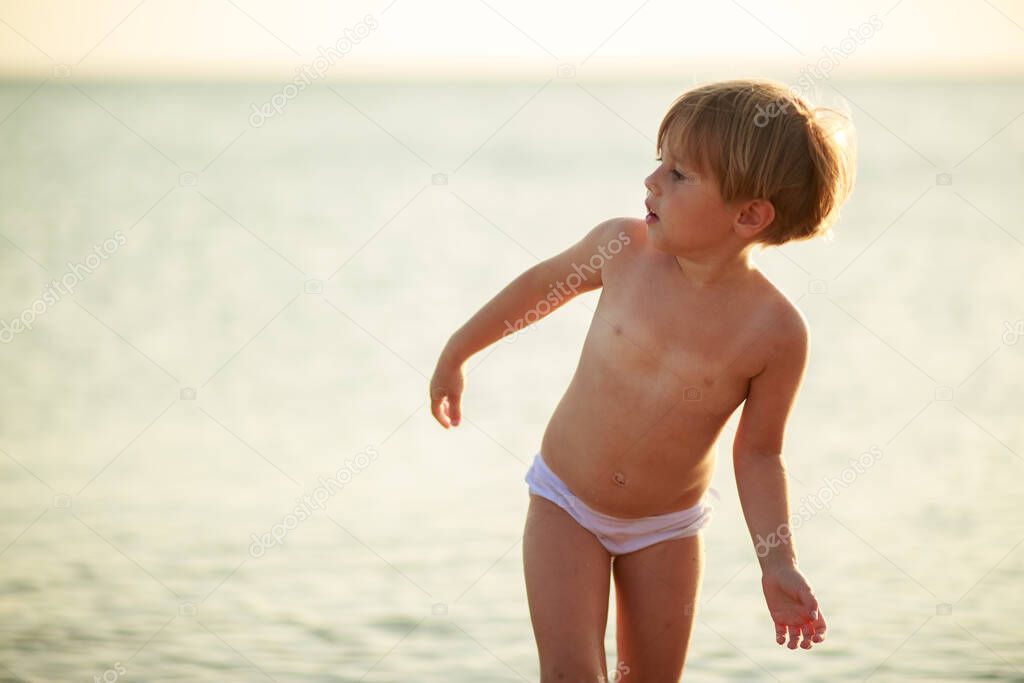 Little cute baby girl in blue short is walking on sunset beach,