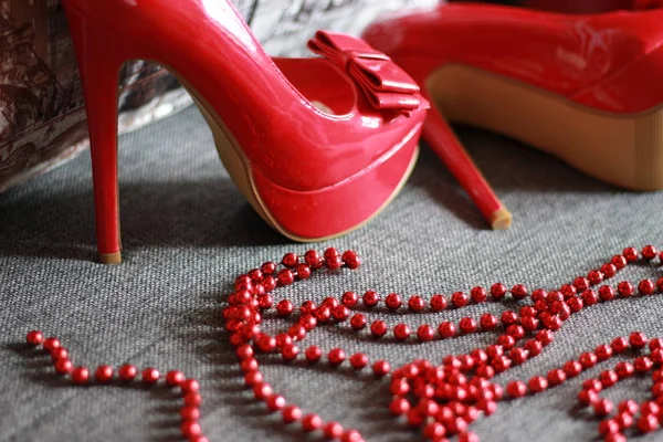 Red high-heeled shoes with beads with a pillow and on the sofa. Stock photography.