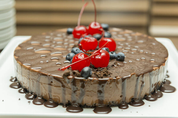 Красивый и вкусный шоколадный десерт с сиропом, вишней и черничной начинкой. Вкусный шоколадный пирог на белом блюде. Концепция изысканной еды. Селективный фокус
.