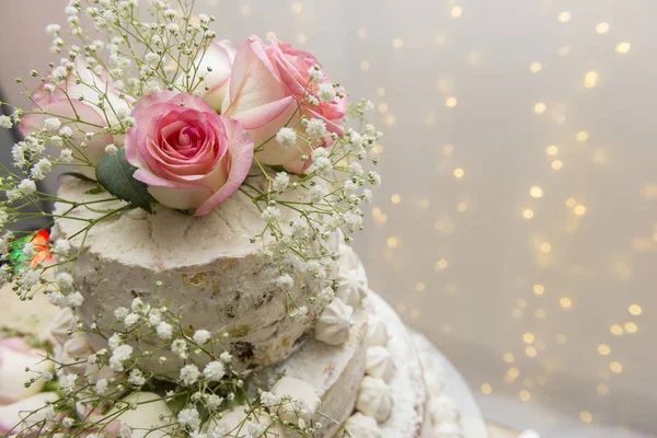 Close up of beautiful white tree tier cake with fresh flowers with fairly light and lanterns glowing in the background on a wooden rustic table. Selective focus. Copy space. — Stock Photo, Image