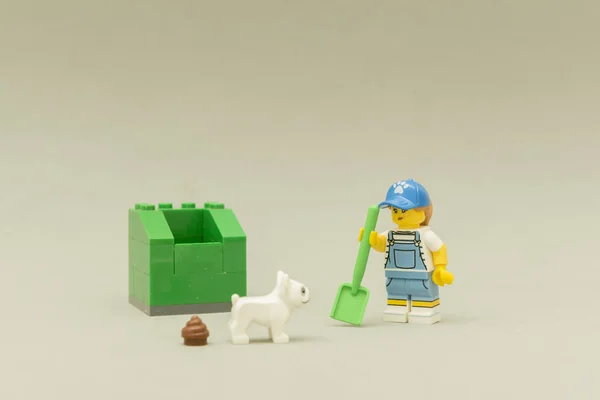 Mujer sosteniendo una pala junto a un cubo de basura verde buscando su caca de perro . — Foto de Stock