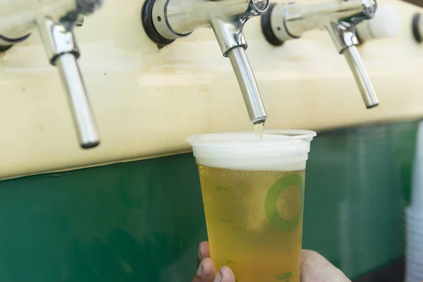 Bartender pouring from tap fresh beer into the plastic cup. Hands of bartender filling beer glass from a bar tap. Hand of bartender pouring a pilsen beer in tap. Street commerce and local culture.