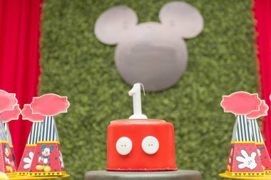 Florianopolis - Brezilya. 2 Şubat 2020: Üzerinde yeşil çim paneli ve kenarlarında kırmızı perde olan bir yıllık bir mum olan güzel bir pasta. Panelde Mickey Mouse şeklinde siyah bir tahta var..