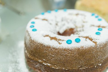 Krema şekerli yalanlarla süslenmiş yuvarlak lezzetli pastaya yaklaş. Pudra şekerli yalanlar serpiştirilmiş yuvarlak bir pasta ve cam beyaz bir masanın üzerine mavi konfeti. Seçici odak.