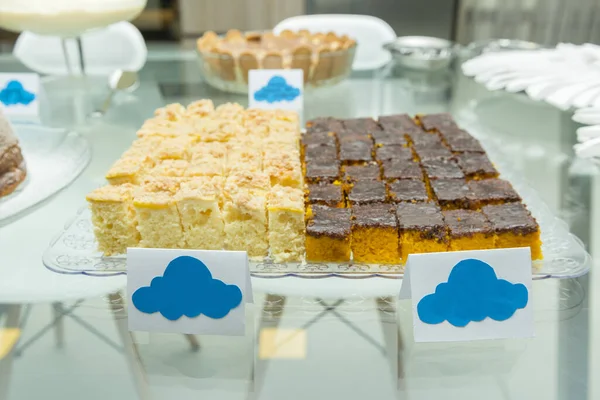 Tray with two types of homemade cakes made by hand. Carrot cake covered with chocolate and cornmeal cake on glass table. Cakes cut into square pieces.