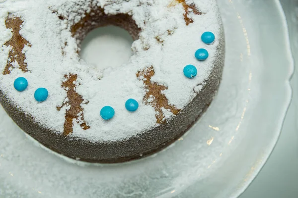 用糖衣装饰的圆圆的美味蛋糕 一个节庆的圆圆的蛋糕撒满了糖粉和蓝色的意大利面 放在一个玻璃白色的桌子上 有选择的重点 — 图库照片