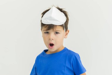 Kafasında cerrahi maske olan ve ağzı açık beyaz bir çocuk salgın tehlikesinden korkuyor. COVID-19. Koronavirüs salgınlarına karşı korunmak için yüz maskesi.