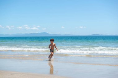 Güneşli bir yaz gününde mavi denizin kıyısında koşan küçük bir çocuk. Brezilya 'nın güzel tropikal plajı. Mavi okyanus ve temiz gökyüzü. Özgürlük kavramı ve eğlenmek. Sahilde izole edilmiş..
