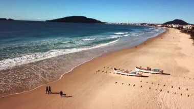 Florianopolis - Brezilya. 24 Mayıs 2020: Brezilya 'da tekir balıkçılığı sırasında plajda egzersiz yapan insanların havadan görüntüsü. Tahta tekneler kıyıya yanaşmış, balıkları bekliyor..