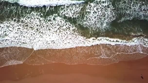 Vue aérienne du mouvement des vagues, des eaux océaniques turquoise avec des vagues s'écrasant sur le rivage créant de beaux motifs tandis que les gens marchent sur le rivage. Zoom arrière - vue aérienne par drone .