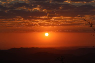 Gün batımındaki dağların manzarası. Arka planda güneş ve bulutlu turuncu gölge.